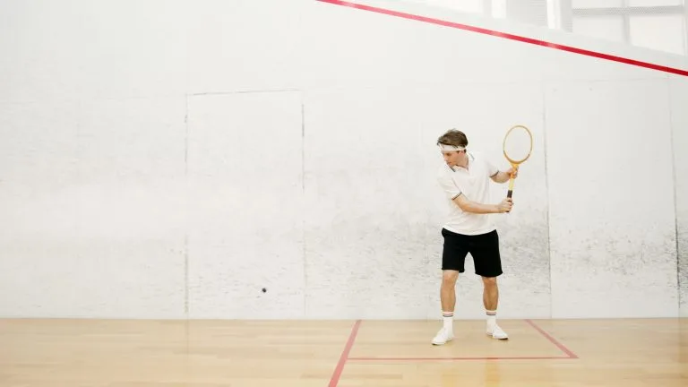 Beginner squash player preparing to return the ball on an indoor court.